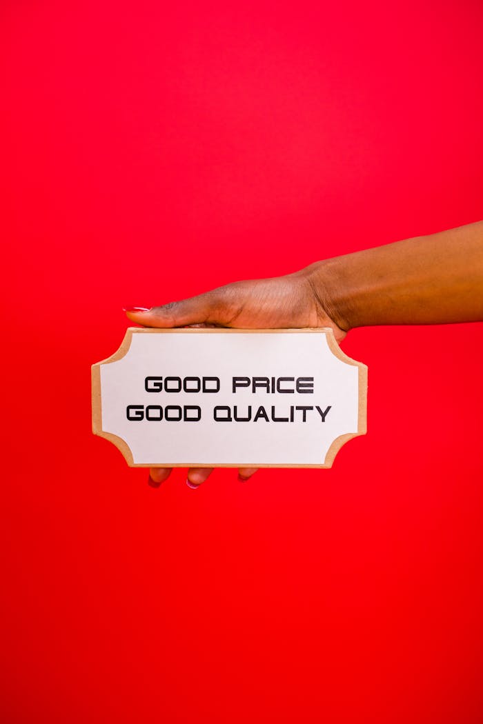 A hand holding a sign with Good Price, Good Quality text against a bright red background.